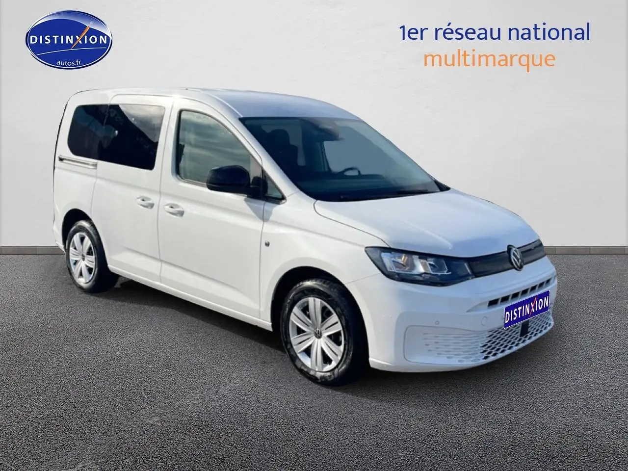Volkswagen Caddy blanc en 3/4 avant droit, avec vitres teintées et jantes alliage visibles.