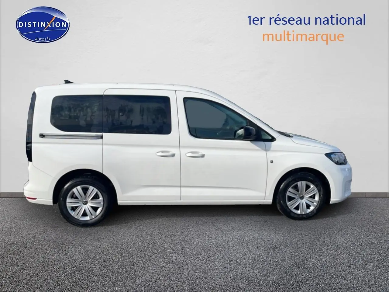 Profil droit d’un Volkswagen Caddy blanc 2025 avec vitres arrière teintées et barres de toit visibles.