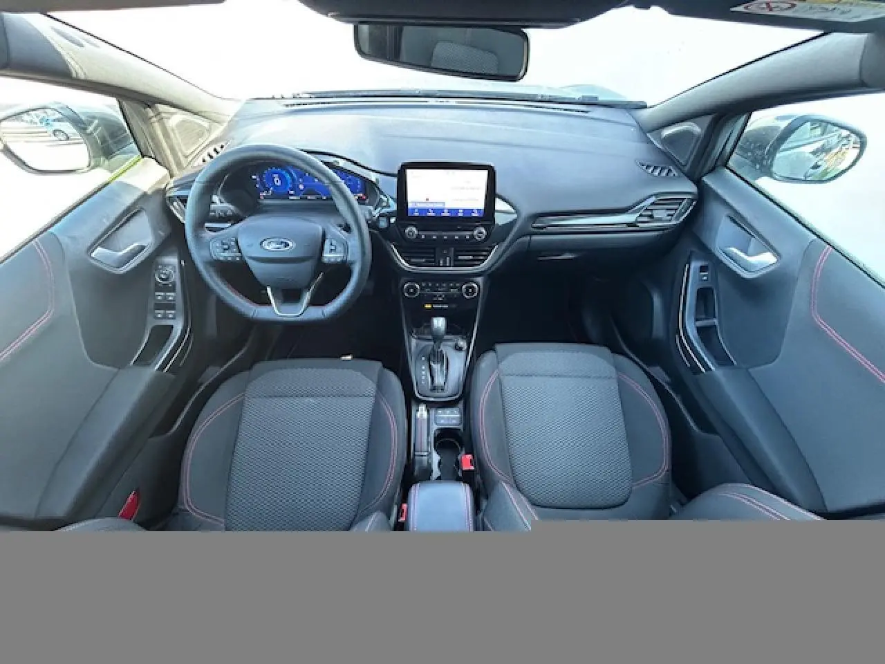 Vue intérieure avant du Ford Puma gris Solar 2023, avec tableau de bord numérique et volant ST-Line à surpiqûres rouges.