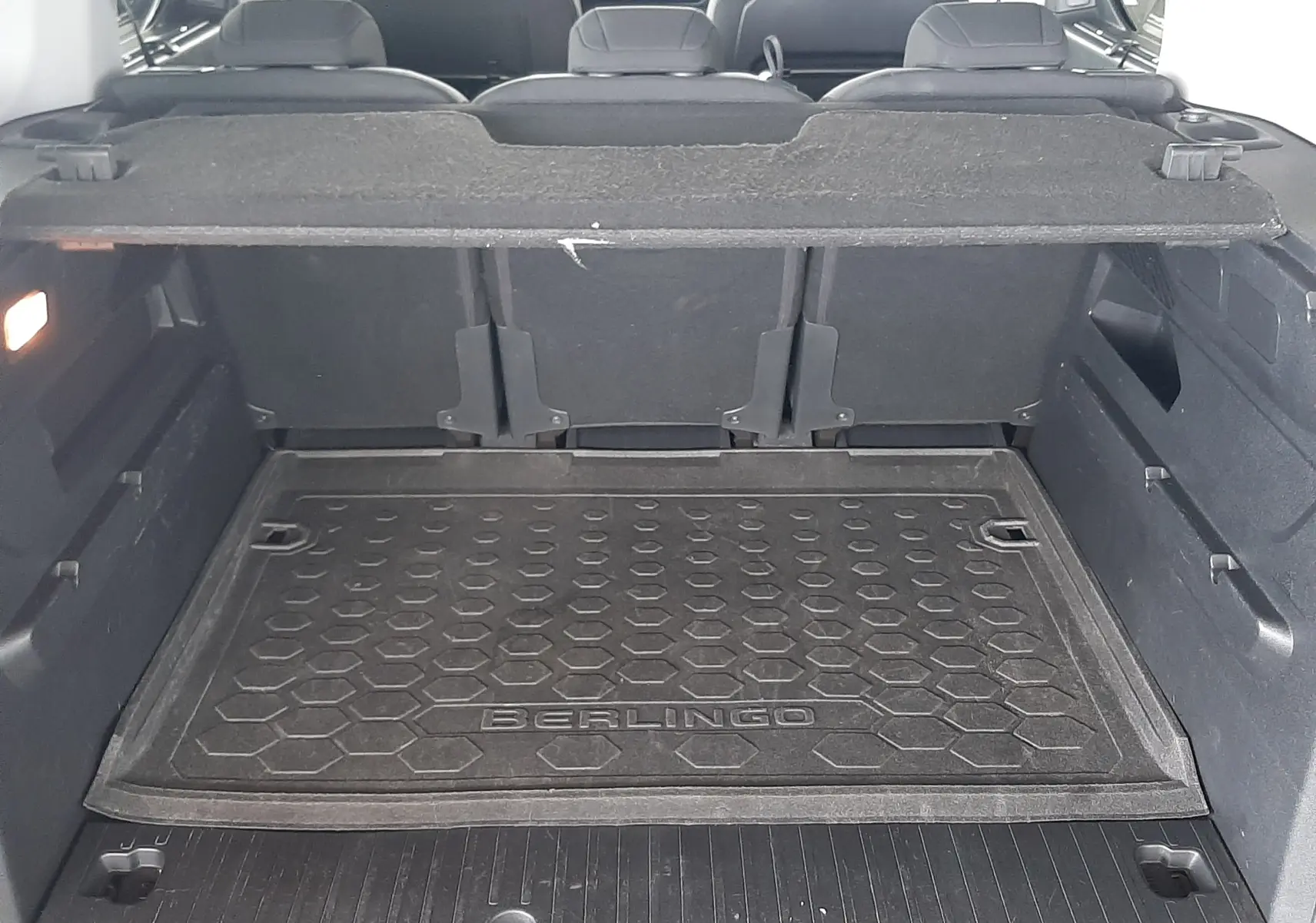 Vue du coffre ouvert d'un Citroën Berlingo 2019 vert, avec tapis de coffre marqué "BERLINGO" et sièges arrière visibles.