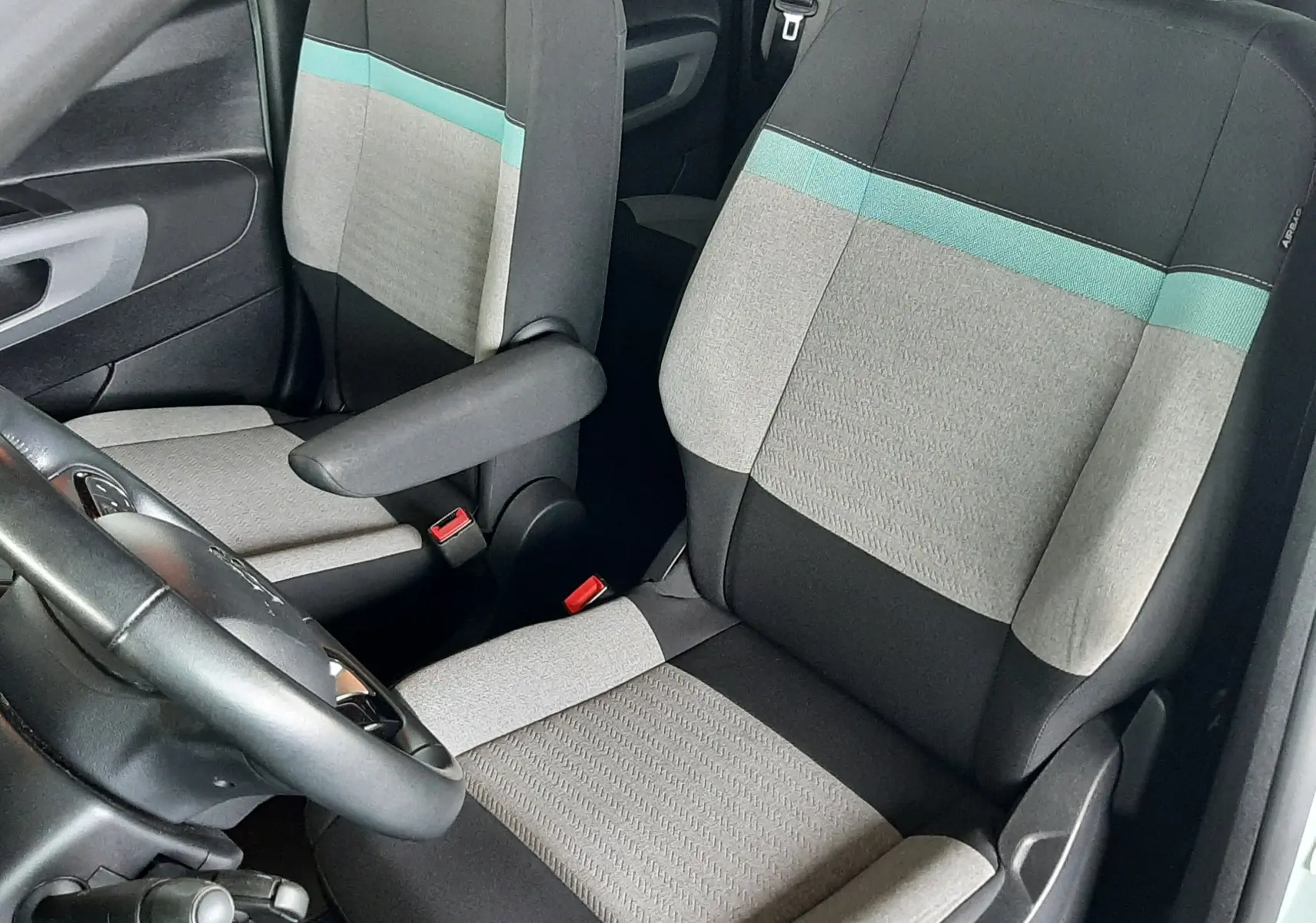 Vue intérieure côté conducteur du Citroën Berlingo 2019, sièges tissu gris clair avec bande turquoise et accoudoir.