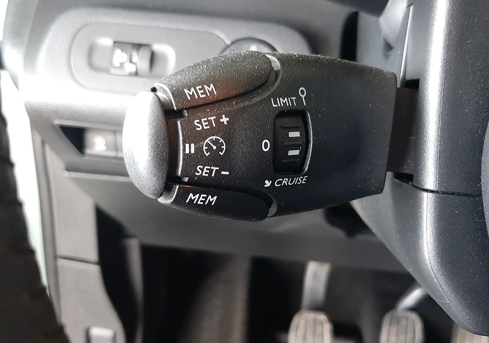 Gros plan sur la commande de régulateur de vitesse noire à gauche du volant dans l’habitacle gris du Citroën Berlingo vert 2019.