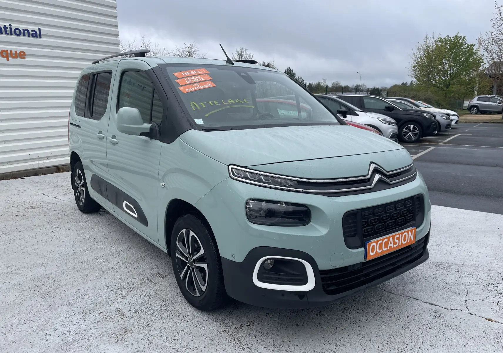 Citroën Berlingo vert clair en 3/4 avant droit, avec stickers orange "Diesel" et plaque "Occasion" visible.