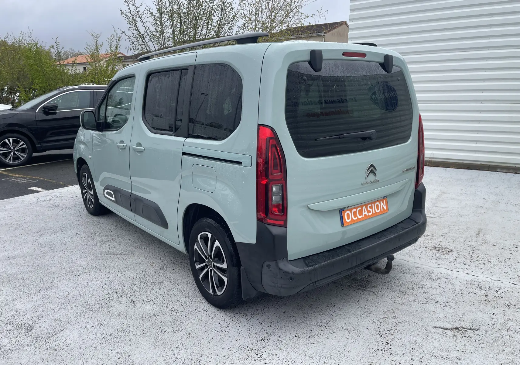 Vue 3/4 arrière droite d'un Citroën Berlingo vert clair 2019 avec hayon, barres de toit et jantes alliage bicolores.