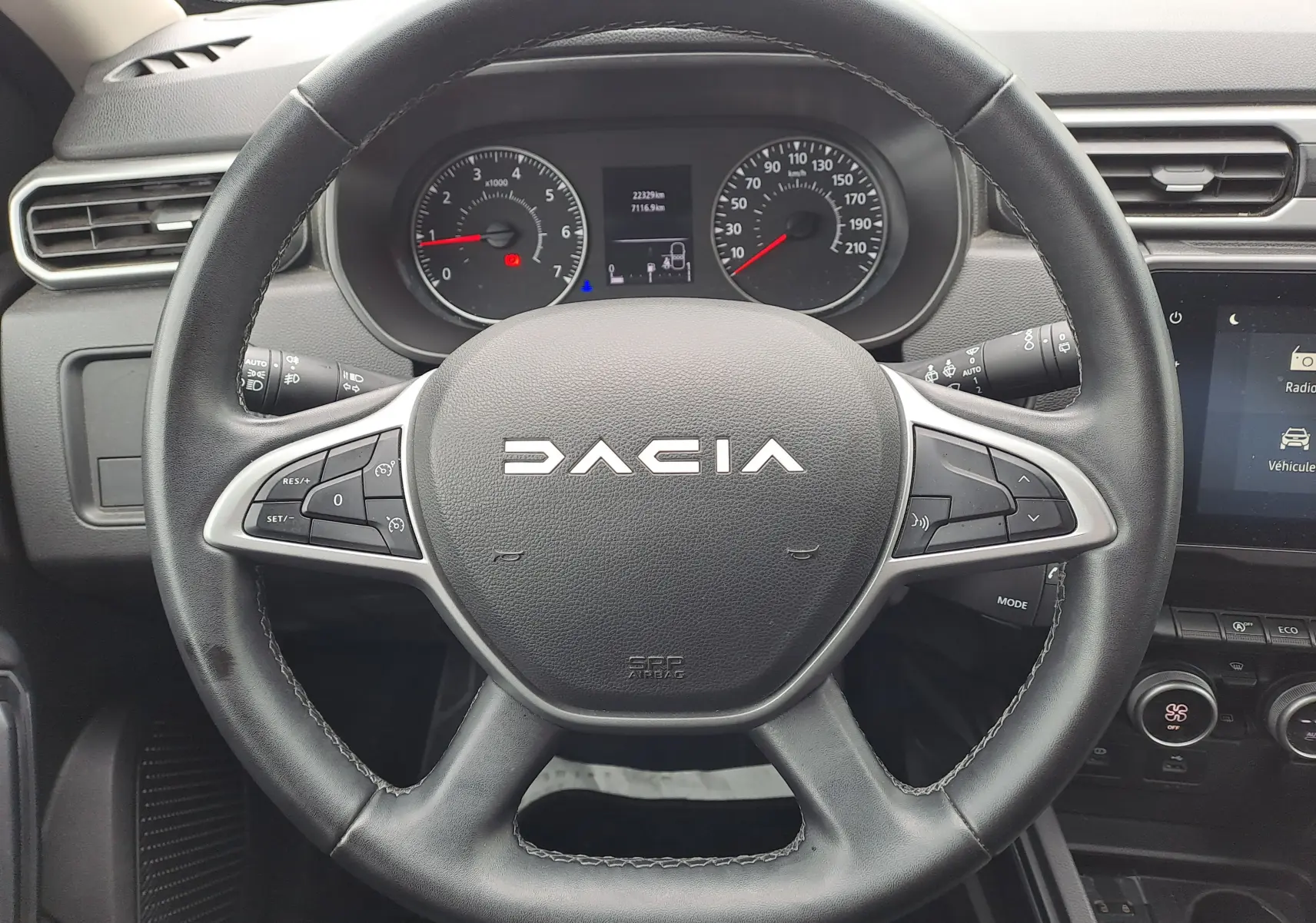 Vue rapprochée du volant noir du Dacia Duster 2024 avec tableau de bord et commandes visibles en arrière-plan.