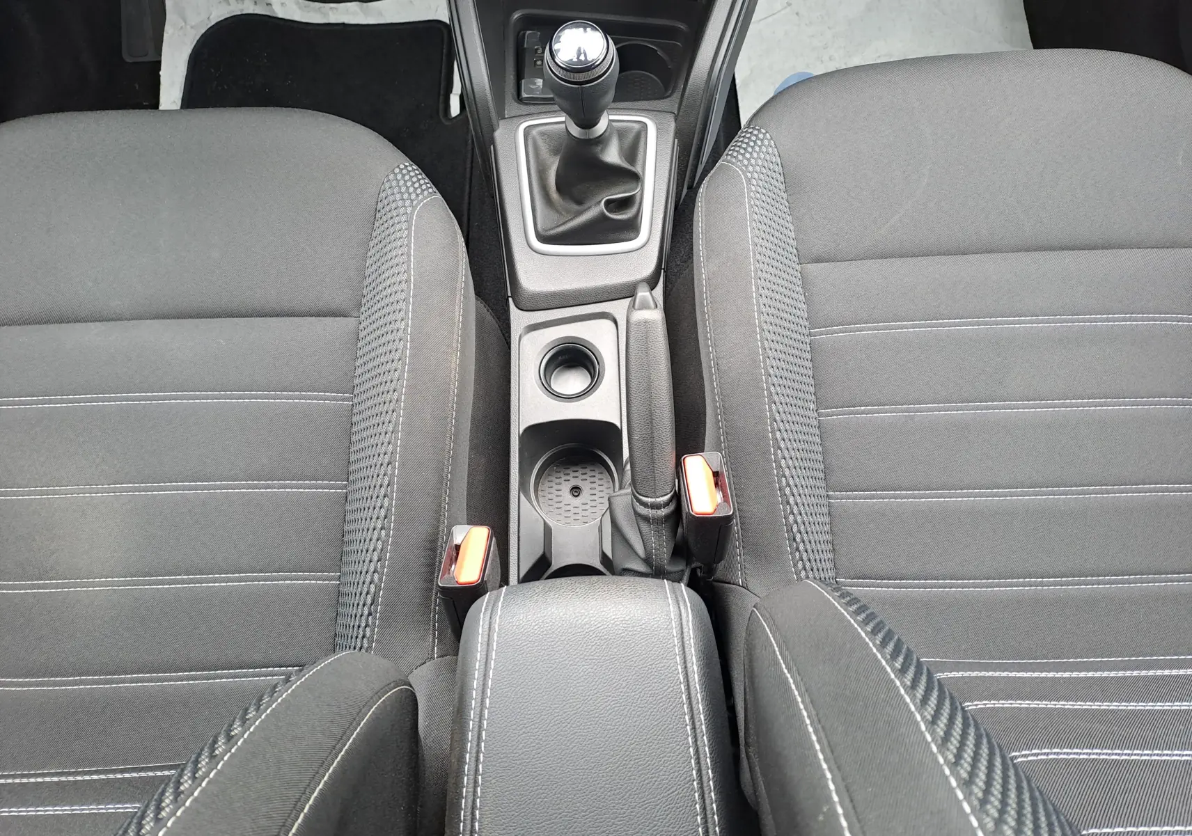 Vue intérieure centrée sur la console centrale et les sièges avant en tissu noir du Dacia Duster 2024 avec boîte manuelle.