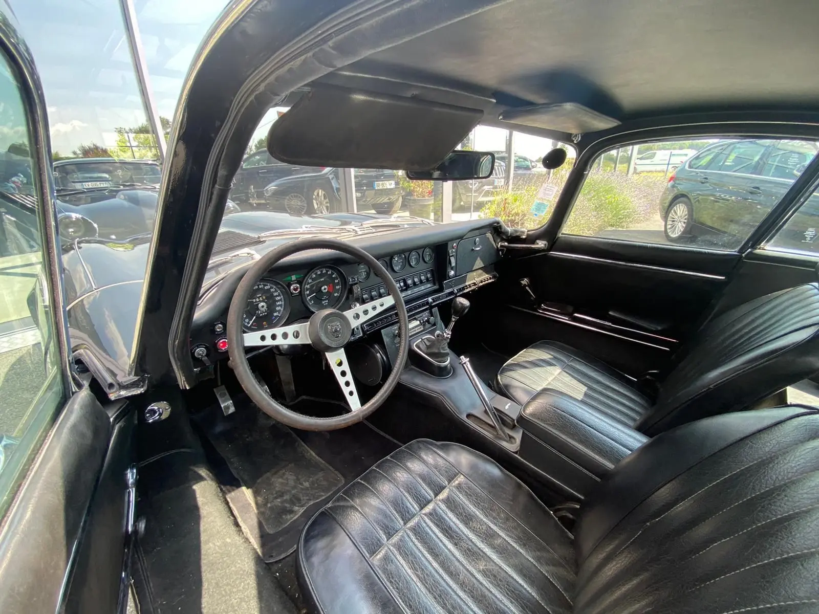 Vue intérieure côté conducteur de la Jaguar S-Type noire de 1970, avec tableau de bord vintage et boîte manuelle.