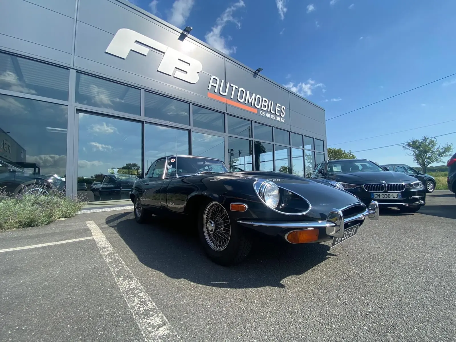 Jaguar Type E Coupé noir 1970 vue 3/4 avant droit, avec jantes à rayons et phares ronds caractéristiques.