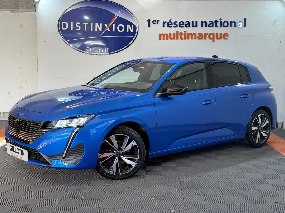 Peugeot 308 bleu en 3/4 avant droit, avec phares LED et jantes alliage distinctives, stationnée en intérieur.