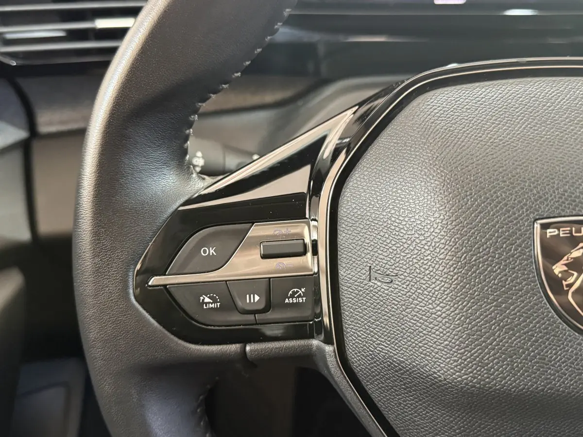 Gros plan sur le volant cuir noir de la Peugeot 308 2023, avec commandes multifonctions et logo lion central.