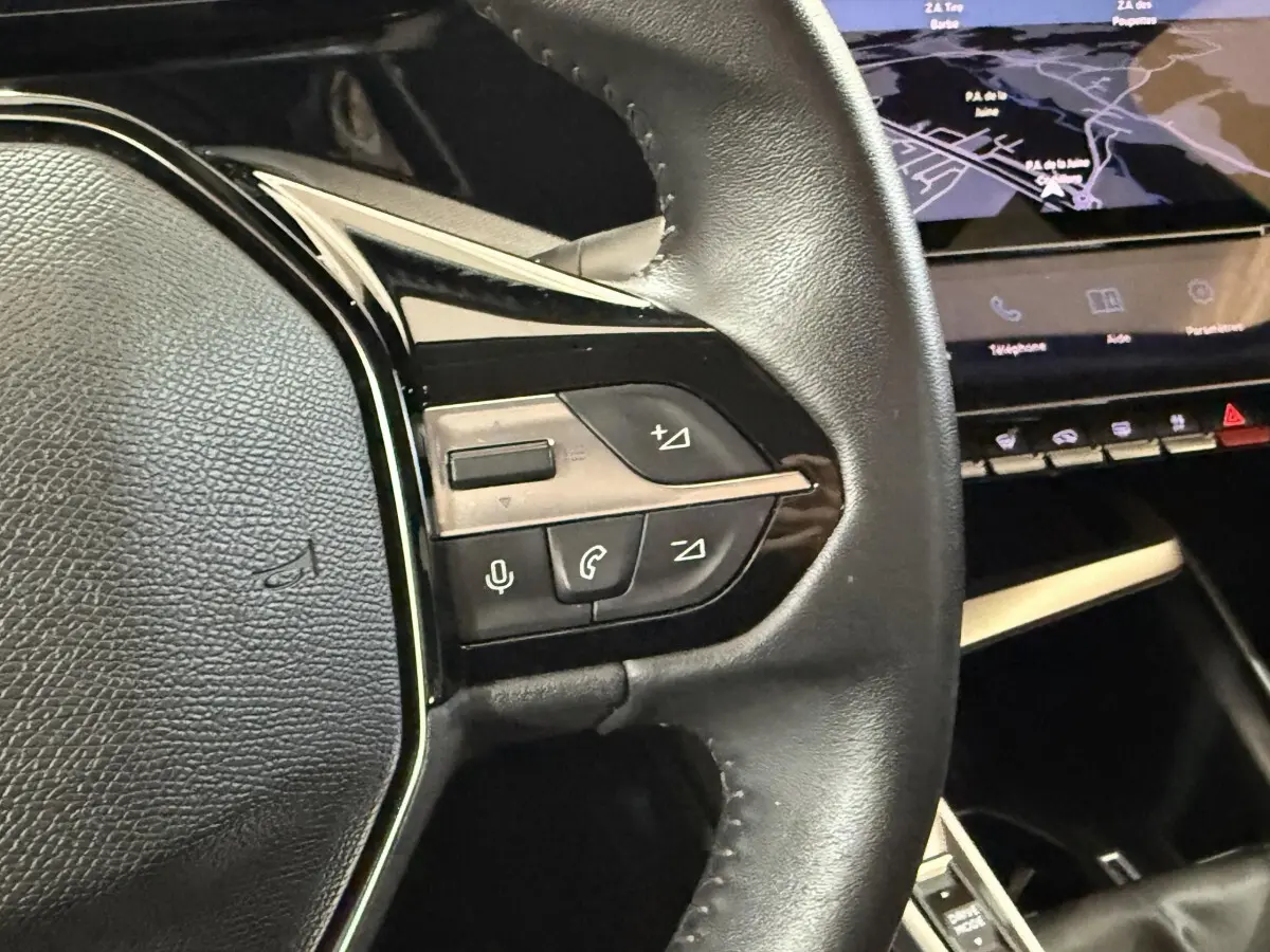 Gros plan sur le volant cuir noir de la Peugeot 308 2023, avec commandes vocales et téléphone visibles.