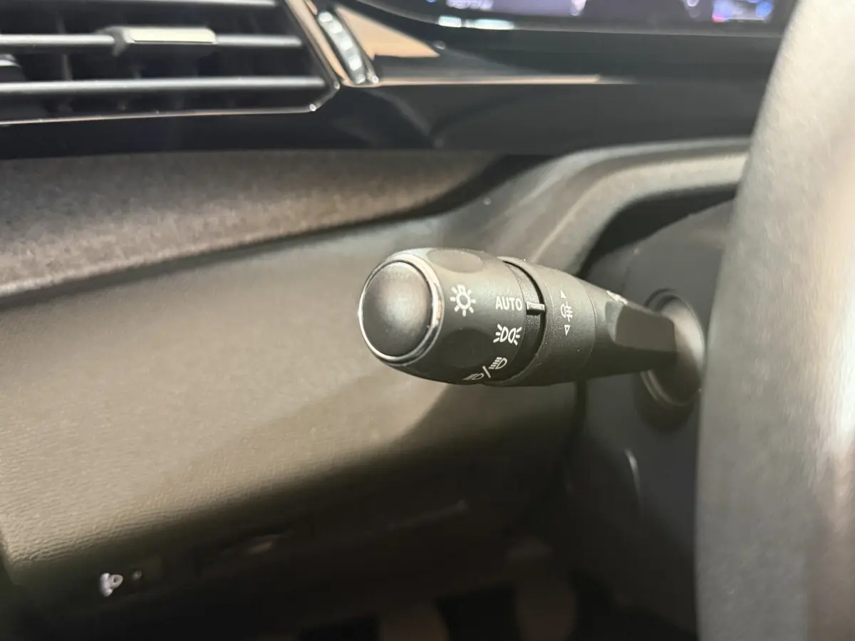 Gros plan sur la commande des phares à gauche du volant dans l’habitacle noir du Peugeot 308 2023 bleu.