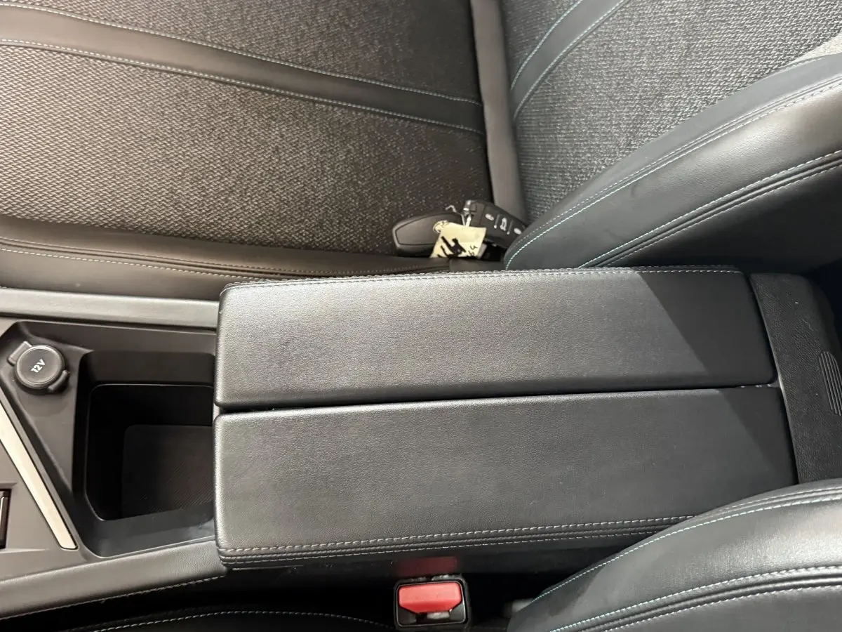Vue rapprochée de l'accoudoir central noir et des sièges en tissu gris foncé à coutures bleues dans une Peugeot 308 2023.