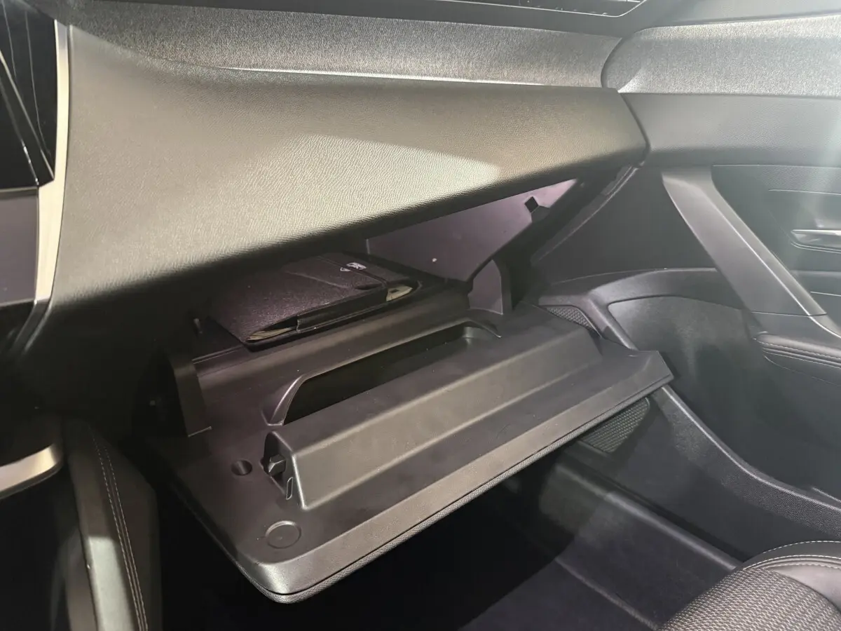 Vue intérieure côté passager du coffre à gants ouvert de la Peugeot 308 bleu, avec un carnet noir à l'intérieur.