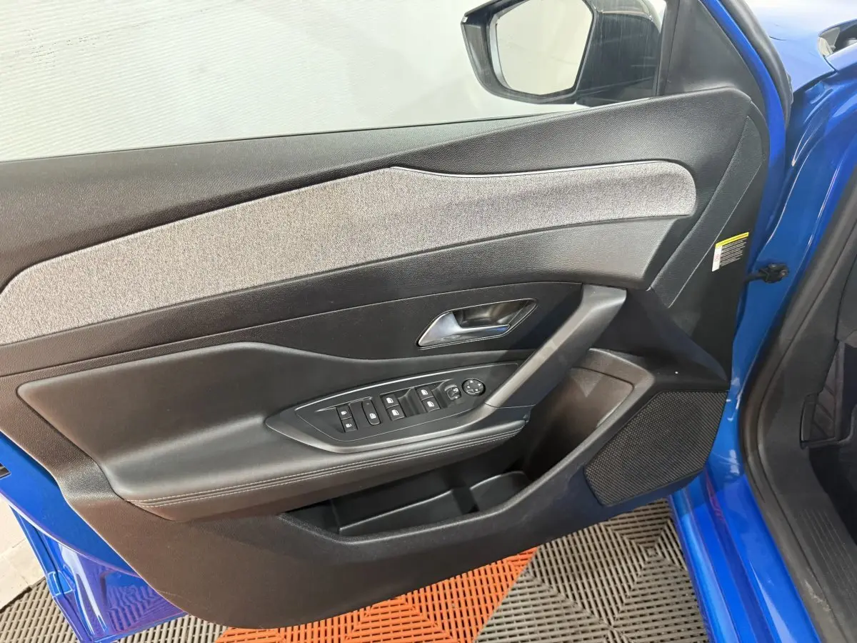 Vue intérieure côté gauche de la porte avant bleu vif d'une Peugeot 308 2023 avec commandes électriques et garniture grise.