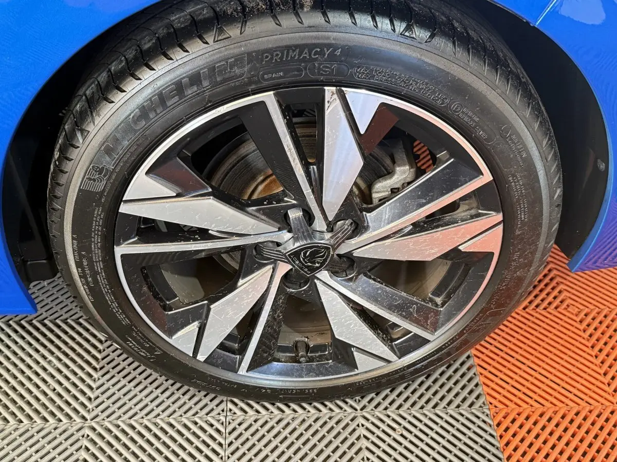 Gros plan sur la roue avant gauche d’une Peugeot 308 bleu 2023 avec jante alliage bicolore et pneu Michelin.