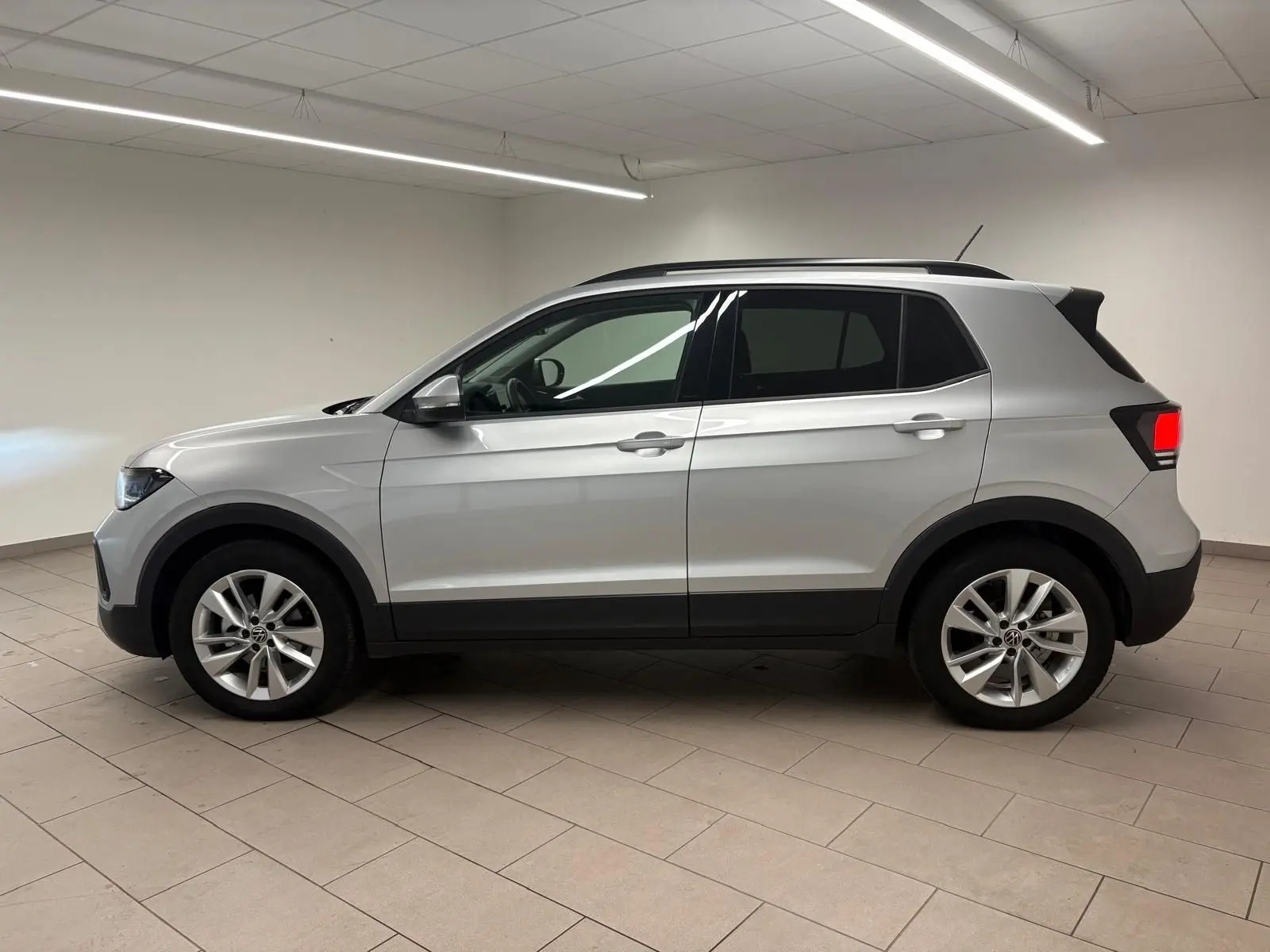 Vue de profil côté gauche d'un Volkswagen T-Cross 2024 en reflet d'argent, avec jantes alliage et vitres surteintées.