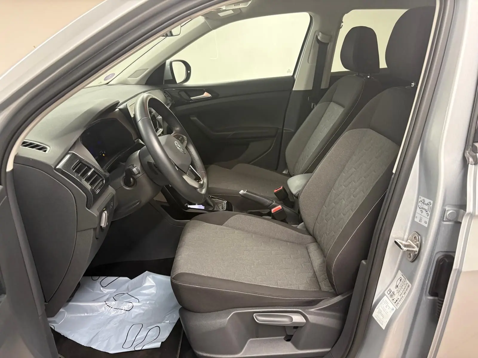 Vue intérieure côté conducteur du Volkswagen T-Cross 2024 argent avec sièges tissu gris et volant multifonction.