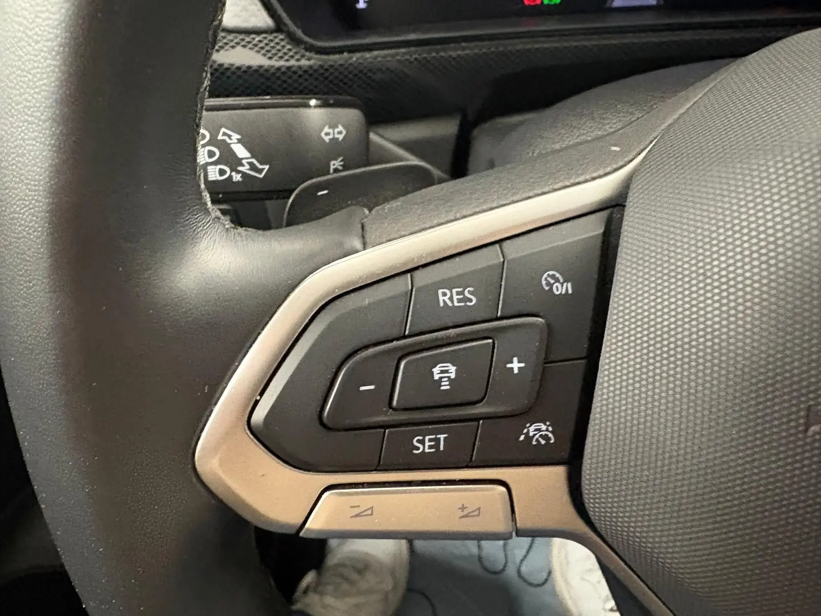 Gros plan sur les commandes du régulateur de vitesse au volant cuir du Volkswagen T-Cross 2024 couleur reflet d'argent.