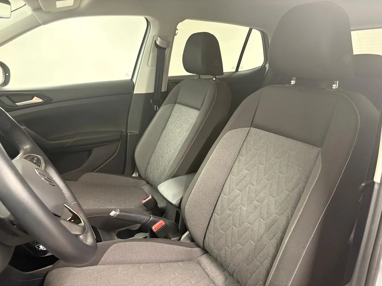 Vue intérieure côté avant droit du Volkswagen T-Cross 2024, sièges tissu gris avec motifs géométriques et accoudoir central.