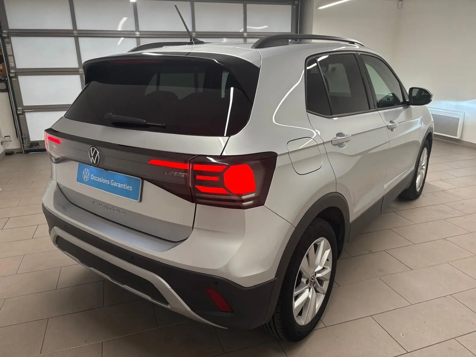 Vue 3/4 arrière droite du Volkswagen T-Cross 2024 en reflet d'argent avec feux arrière allumés dans un garage.