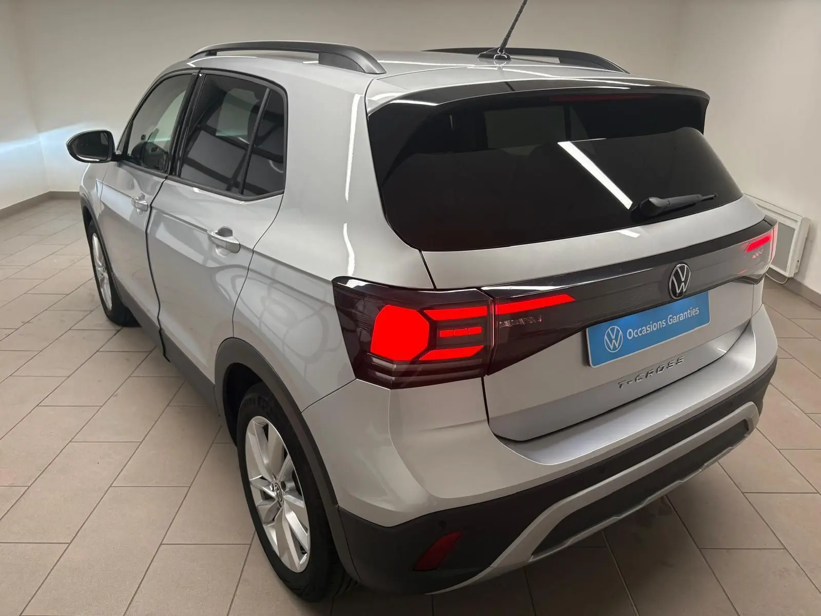 Vue 3/4 arrière droite du Volkswagen T-Cross 2024 en reflet d'argent avec feux arrière LED allumés et vitres surteintées.