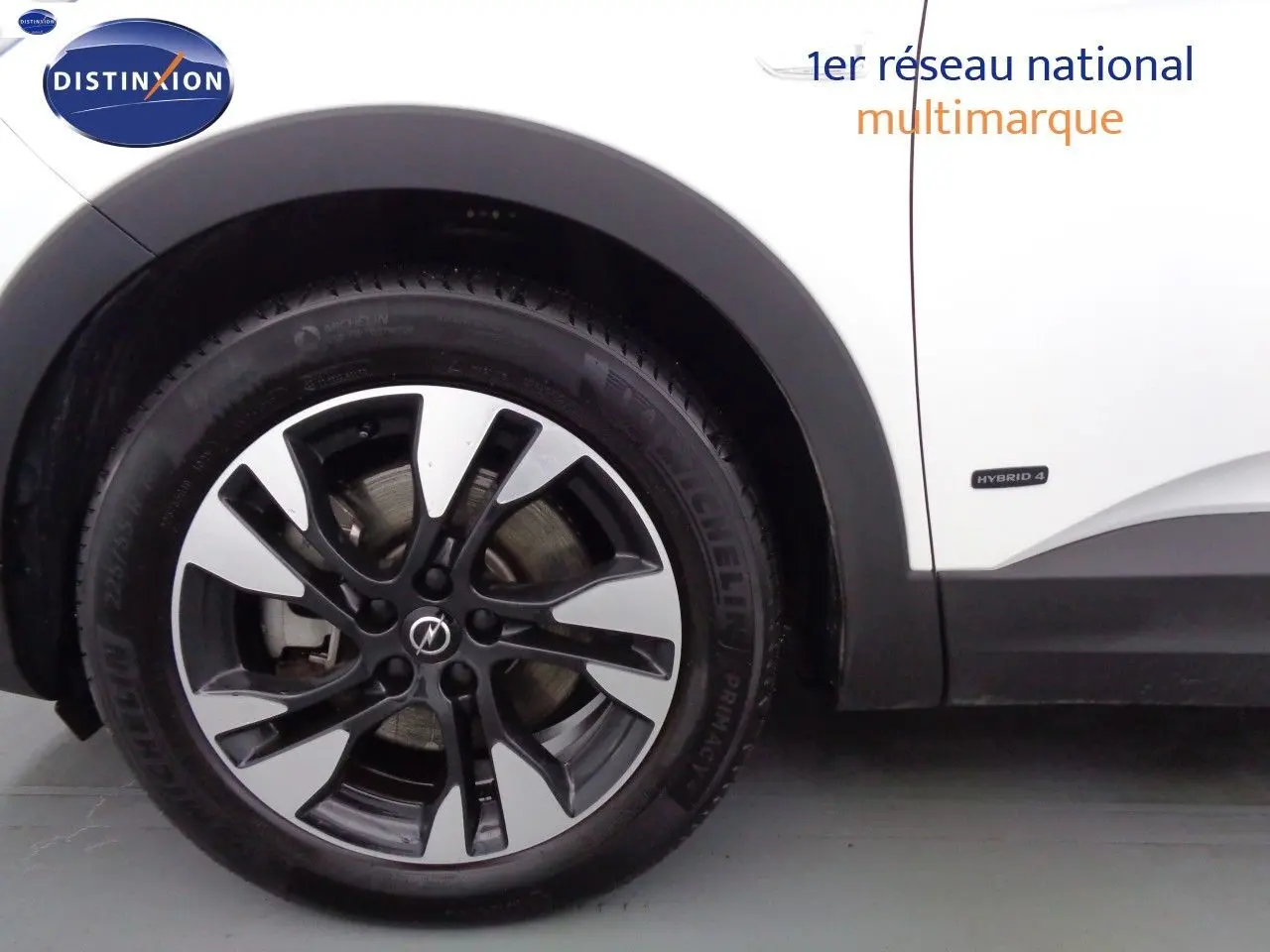 Gros plan sur la roue avant gauche d'un Opel Grandland X blanc nacré avec badge Hybrid 4 sur la carrosserie.