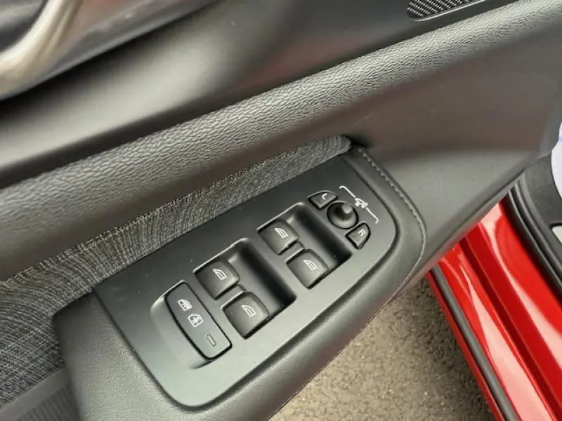 Gros plan sur les commandes des vitres et rétroviseurs côté conducteur d'une Volvo S60 rouge fusion métallisé 2024.