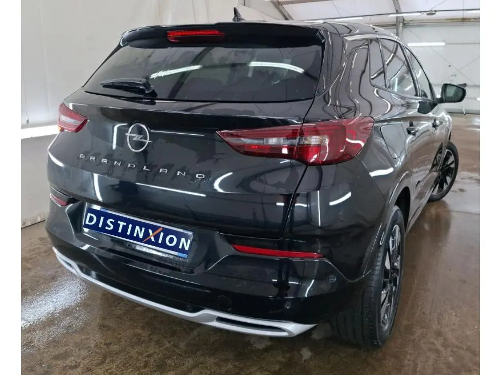 Opel Grandland noir vue de profil côté gauche, jantes alliage bicolores, intérieur showroom avec mur orange.