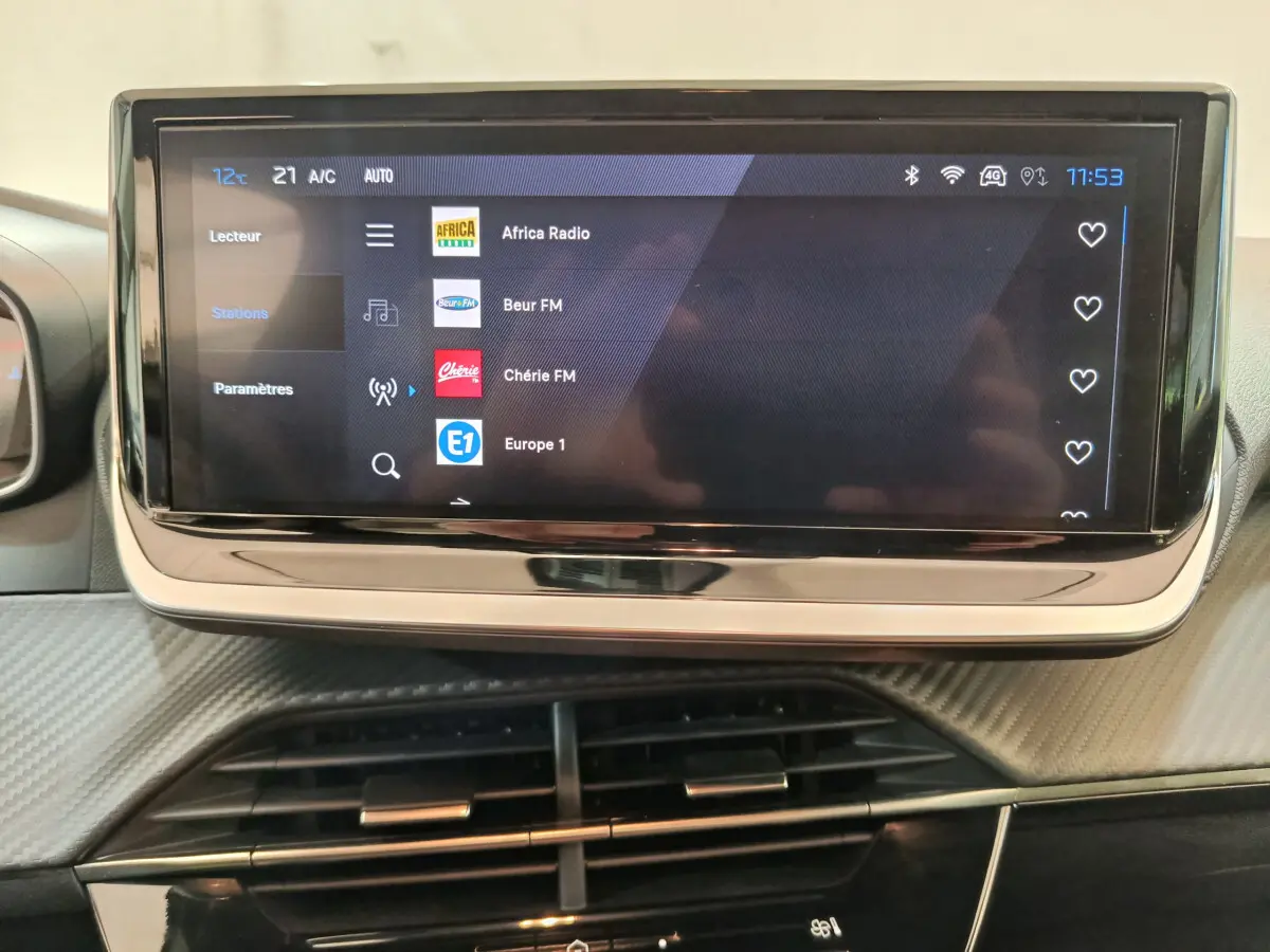 Écran tactile central de la Peugeot 208 gris clair, affichant les stations radio, vue intérieure frontale.