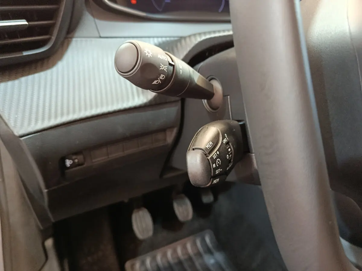 Gros plan sur commandes au volant et levier de clignotant dans l’habitacle gris foncé d’une Peugeot 208 2025.