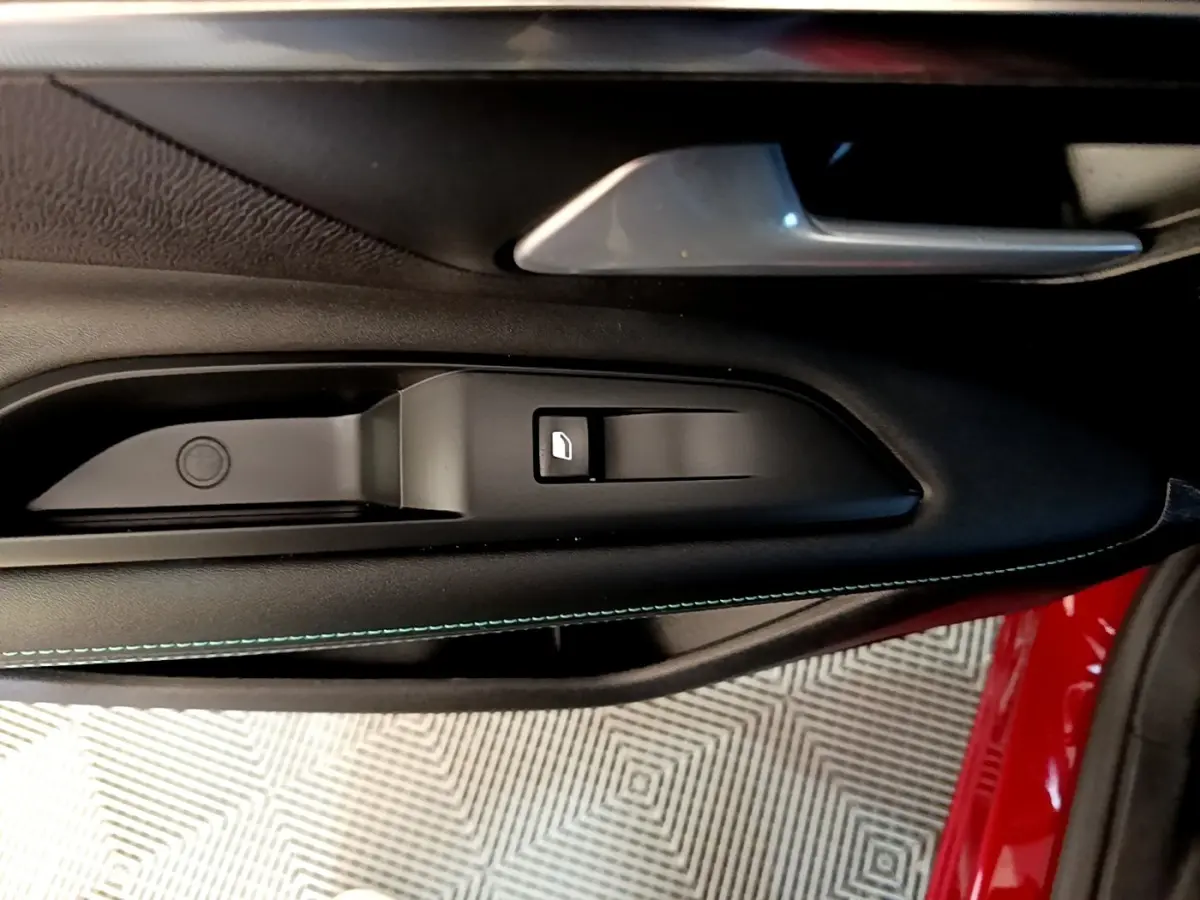 Gros plan sur la commande de lève-vitre côté gauche intérieur d'une Peugeot 3008 rouge avec surpiqûres bleues.