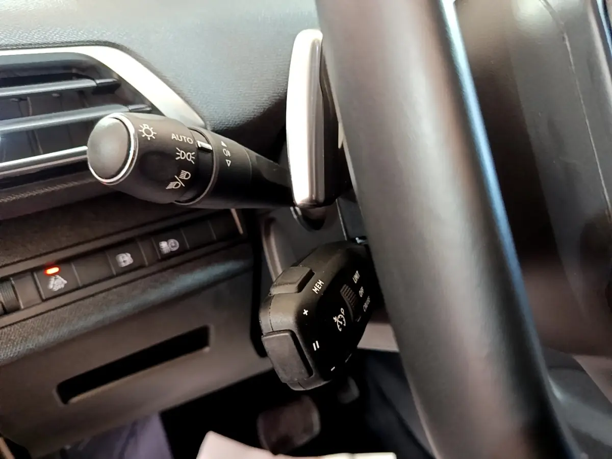 Vue rapprochée du volant noir et des commandes de phares et régulateur de vitesse du Peugeot 3008 hybride rechargeable 2021.