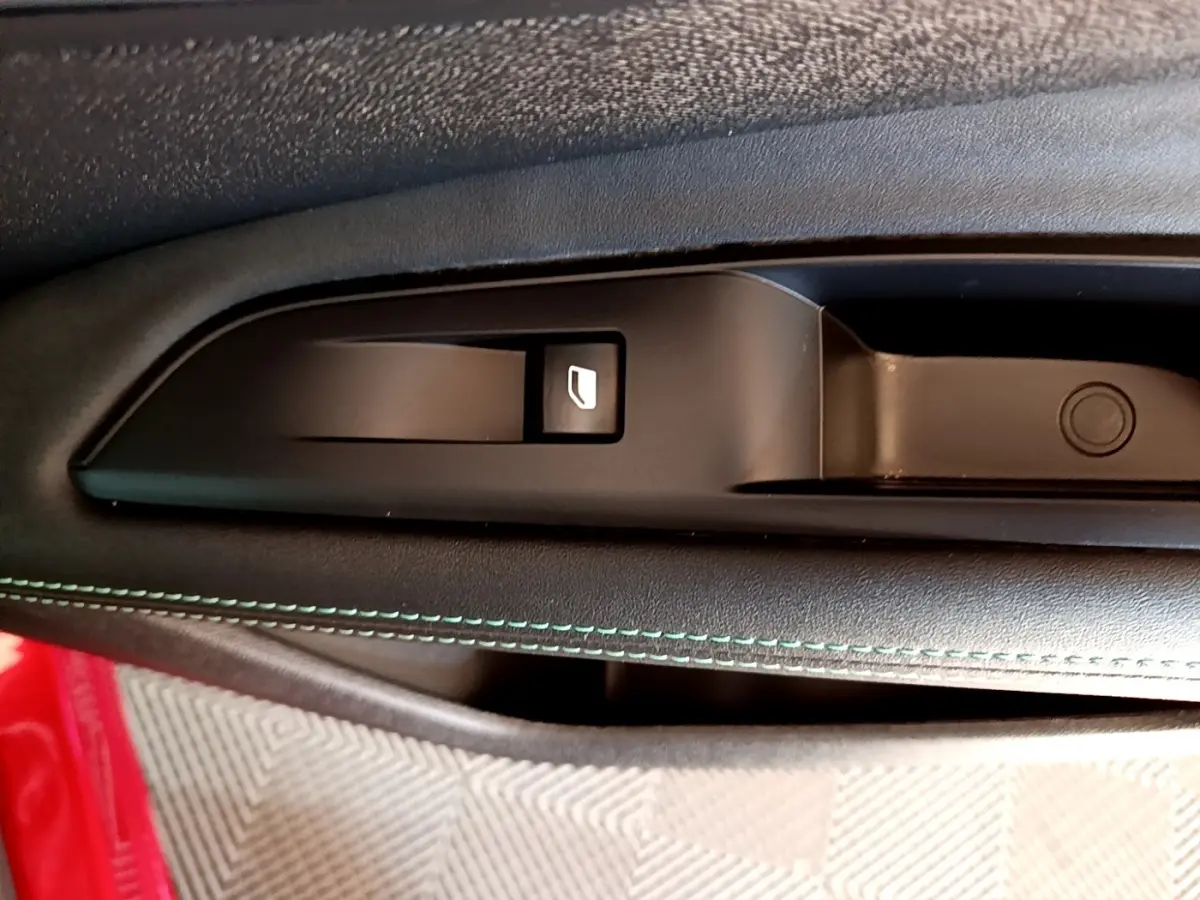 Gros plan sur la commande de lève-vitre côté conducteur avec surpiqûres vertes sur la portière noire du Peugeot 3008 hybride.
