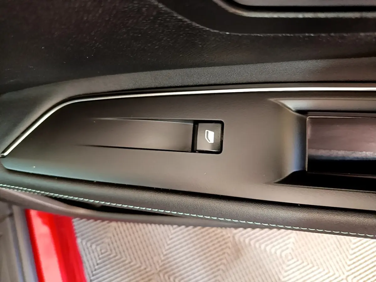 Détail de la poignée intérieure noire avec bouton d’ouverture sur la porte côté conducteur d’un Peugeot 3008 rouge.