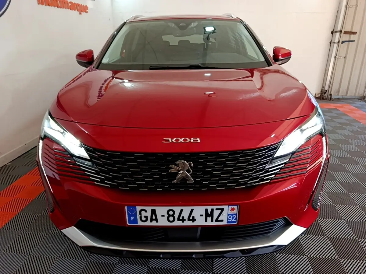 Vue avant d'un Peugeot 3008 hybride rechargeable rouge avec calandre noire et phares LED allumés dans un garage.