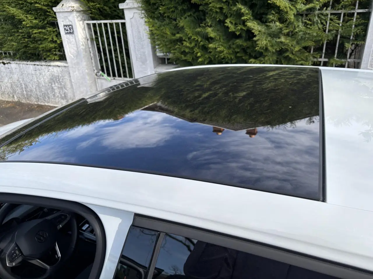 Toit panoramique noir sur une Volkswagen Golf blanche 2024, vue plongeante sur l'avant côté gauche avec intérieur visible.