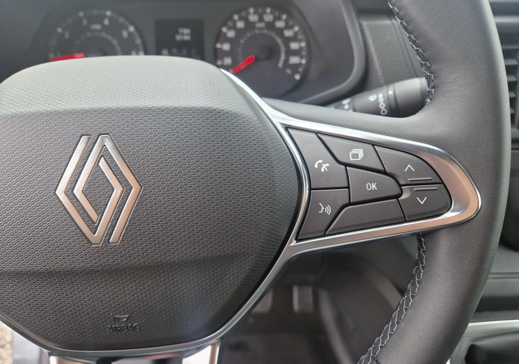 Gros plan sur le volant noir du Renault Trafic Fourgon 2025 avec commandes intégrées et logo Renault central.