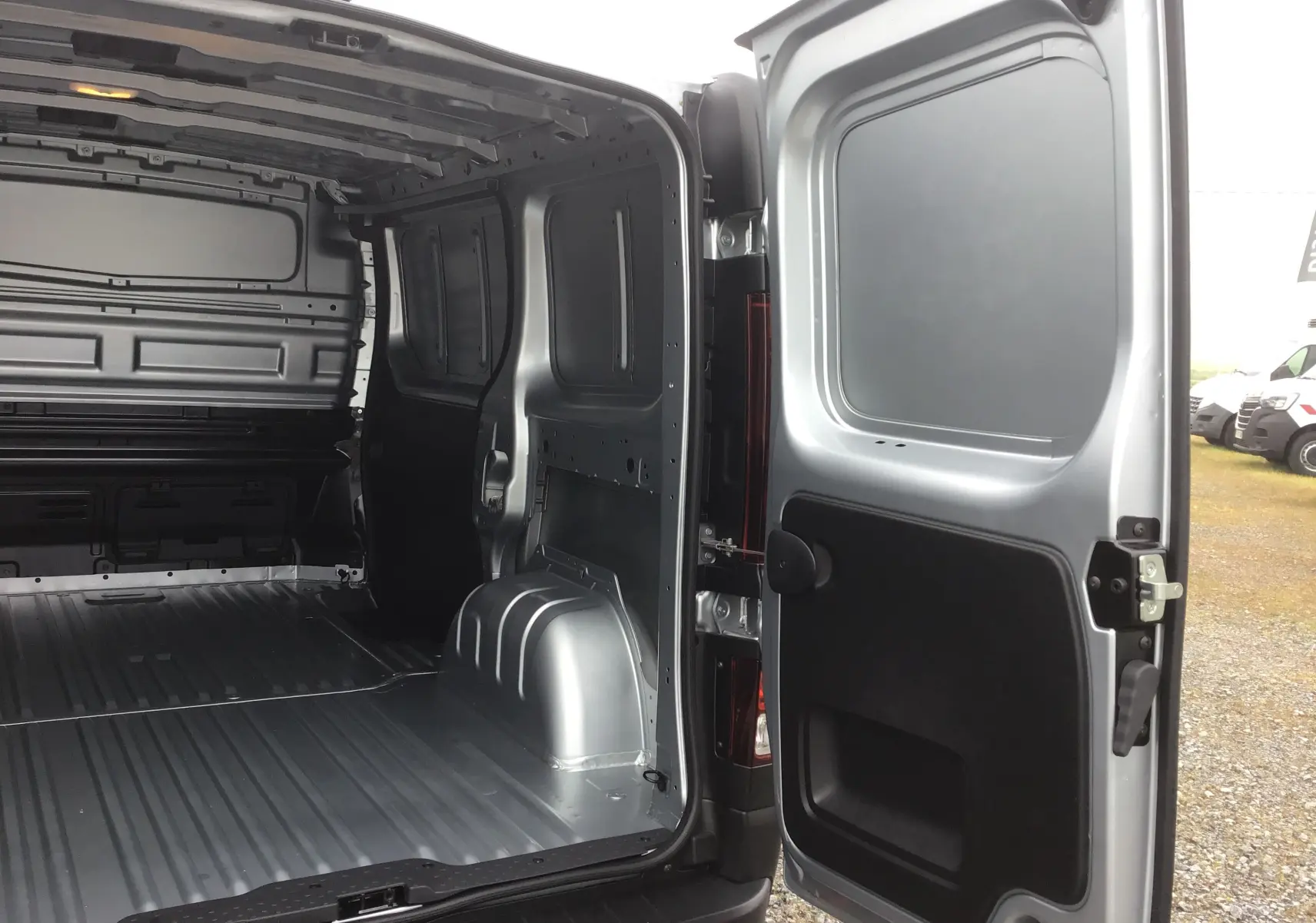 Vue intérieure arrière du Renault Trafic Fourgon gris Highland 2025, montrant l'espace de chargement vide et la porte ouverte côté droit.
