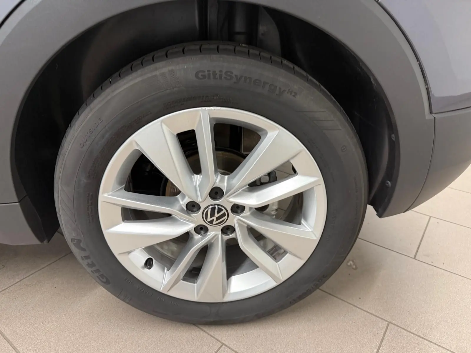 Gros plan sur la roue avant droite d’un Volkswagen T-Cross gris cendre, mettant en valeur la jante alliage et le pneu GitiSynergy.