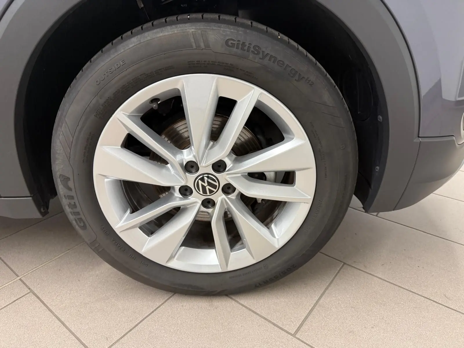 Gros plan sur la roue avant gauche du Volkswagen T-Cross gris cendre, mettant en valeur la jante alliage à 10 branches.