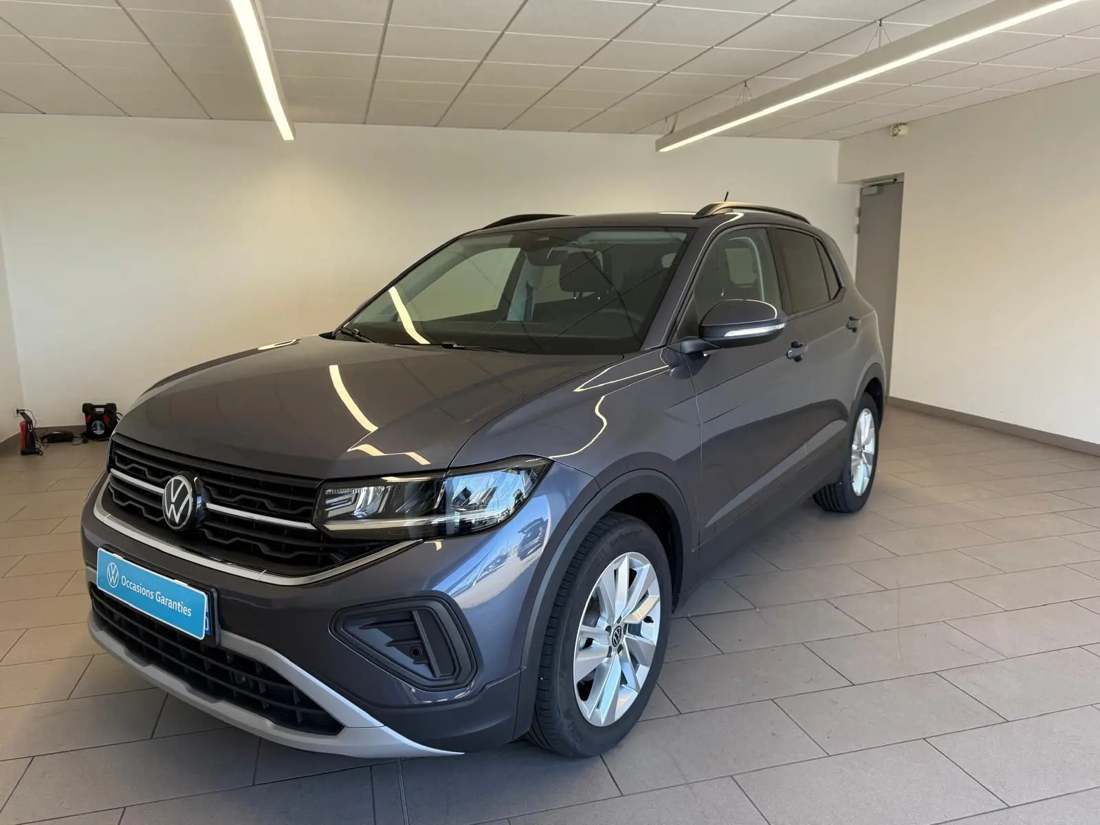 Volkswagen T-Cross gris cendre en 3/4 avant droit, avec calandre noire et jantes argentées, dans un showroom lumineux.