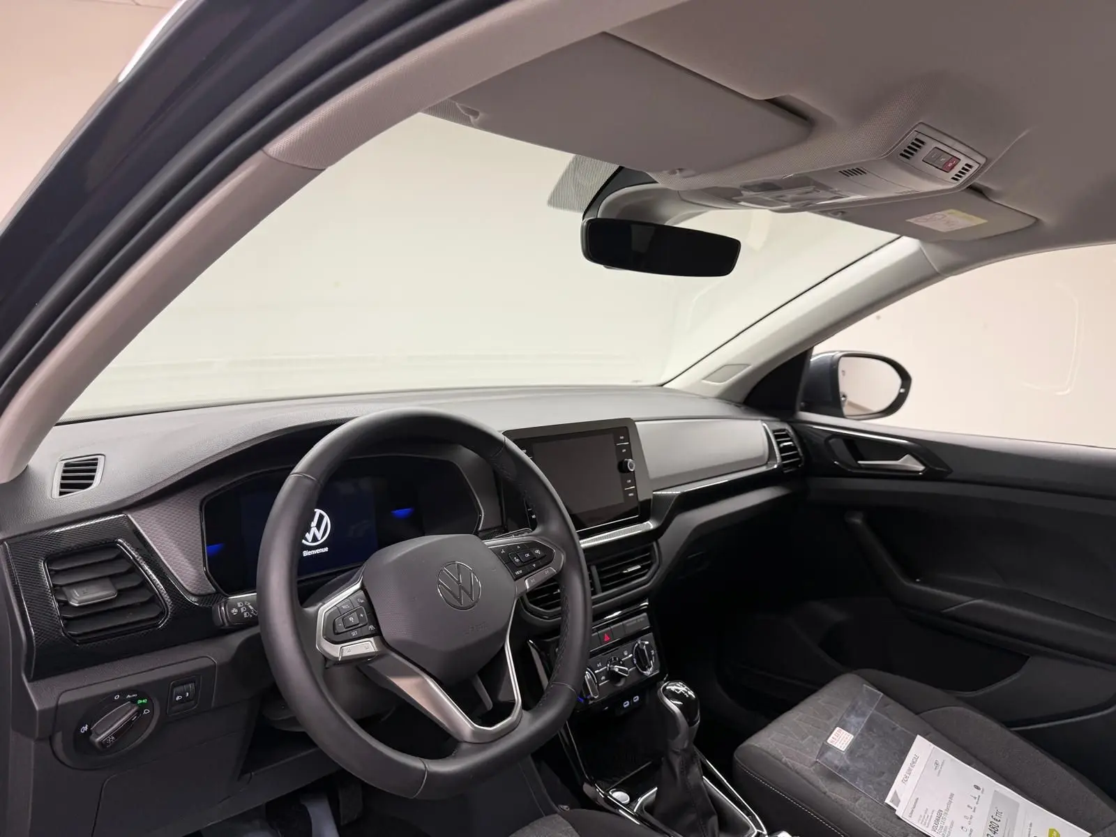 Vue intérieure côté conducteur du Volkswagen T-Cross gris cendre 2025, avec volant multifonction et écran tactile central.