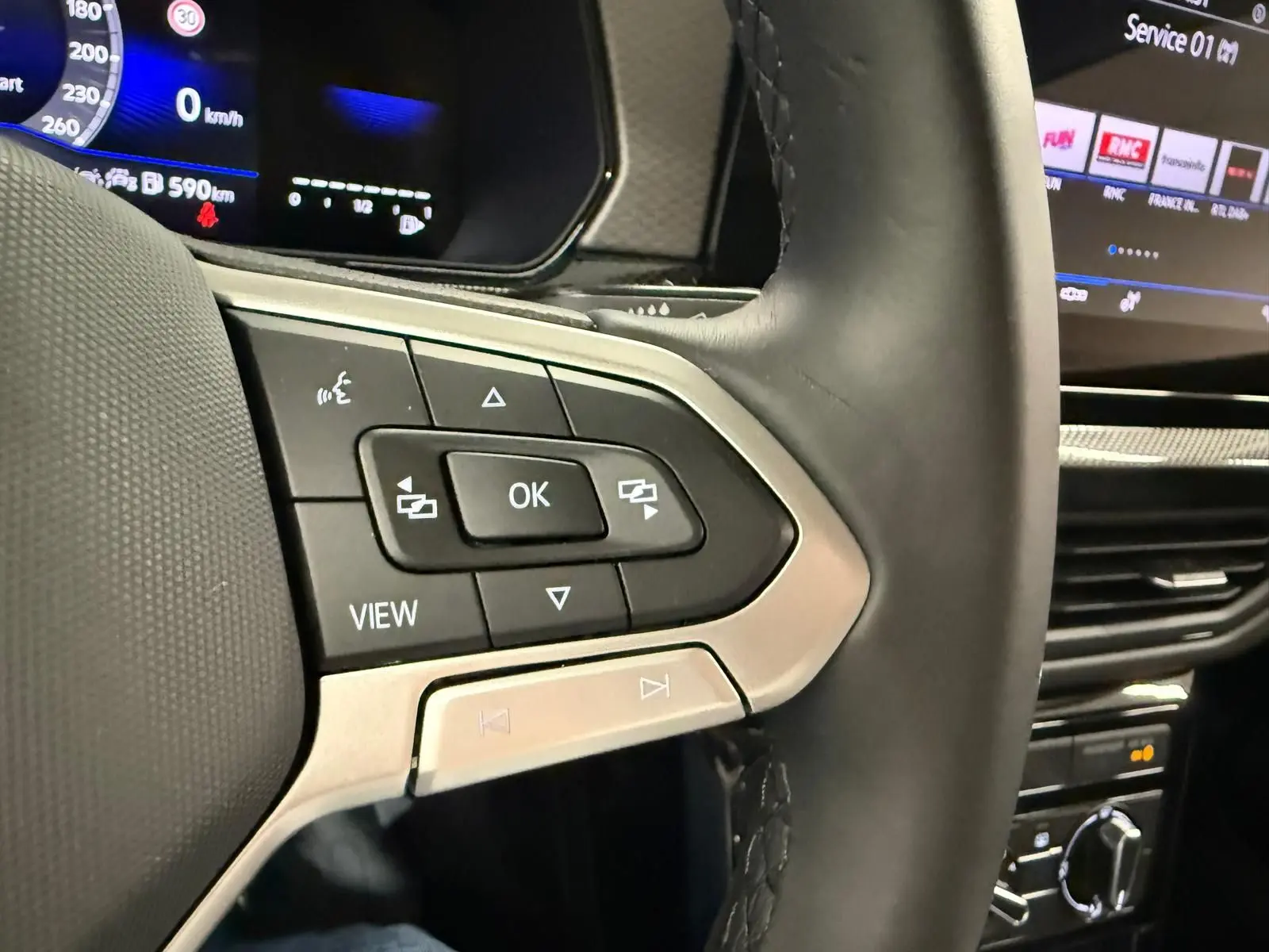 Gros plan sur le volant côté gauche du Volkswagen T-Cross gris cendre 2025, avec commandes multifonctions et tableau de bord numérique.