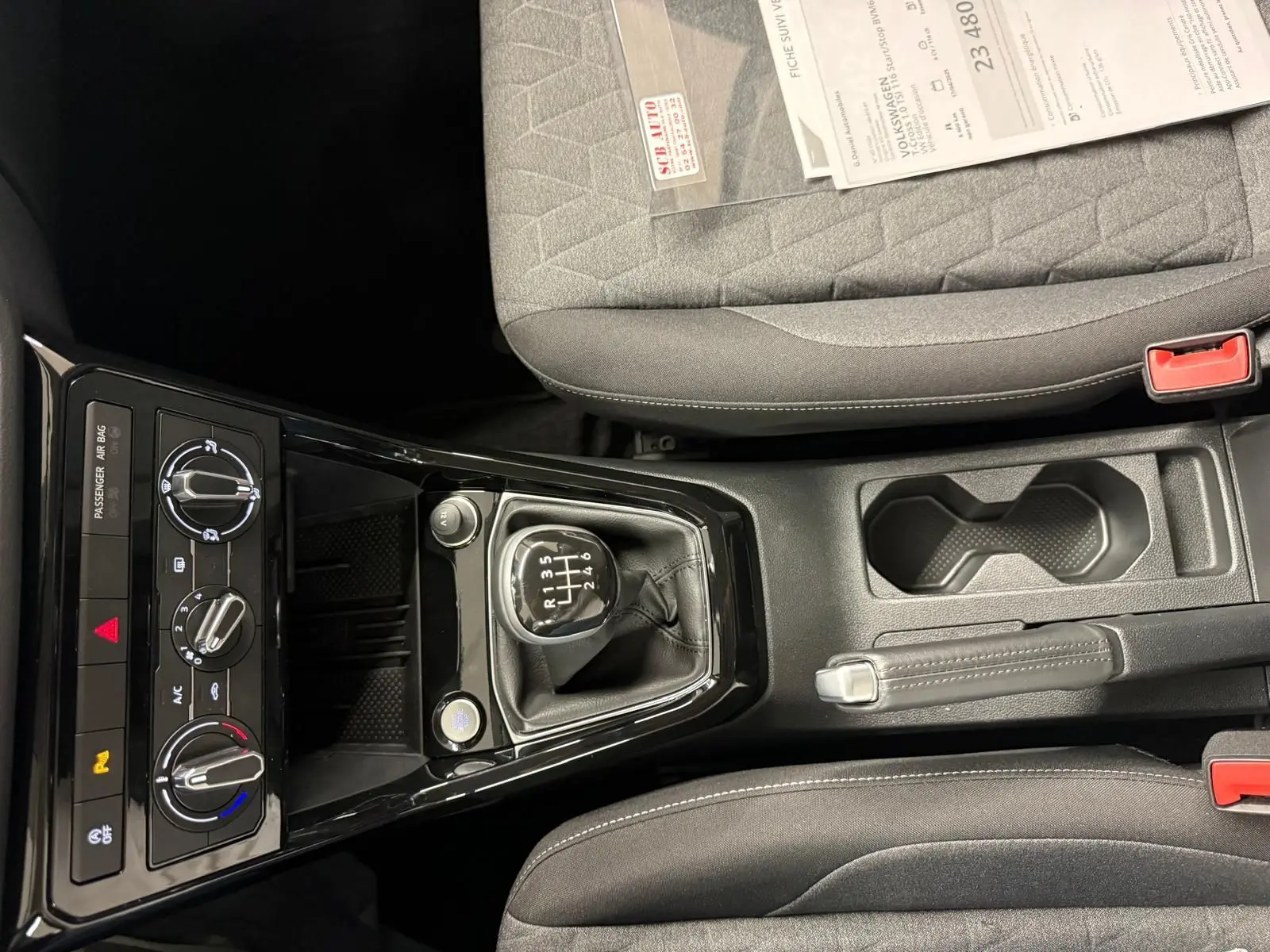 Vue intérieure centrée sur la console centrale du Volkswagen T-Cross gris cendre, avec levier de vitesse manuel et commandes climatisation.