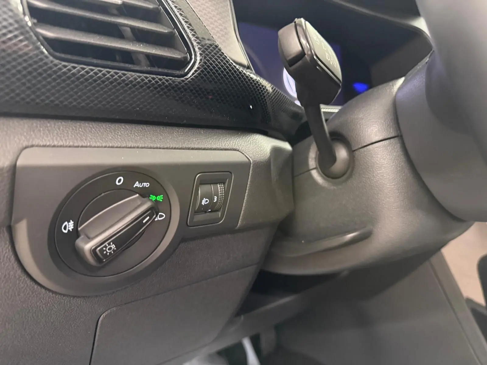 Détail du tableau de bord côté gauche du Volkswagen T-Cross gris cendre 2025, avec commande des phares et régulateur de hauteur.