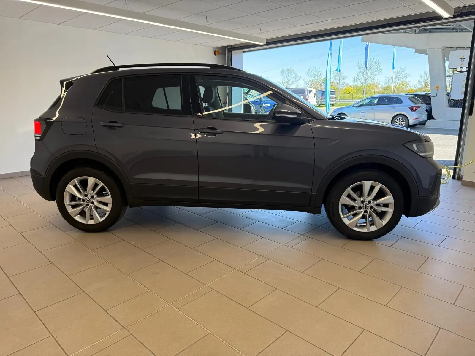 Profil côté gauche du Volkswagen T-Cross gris cendre 2025, version 1.0 TSI VW Edition, en intérieur lumineux.