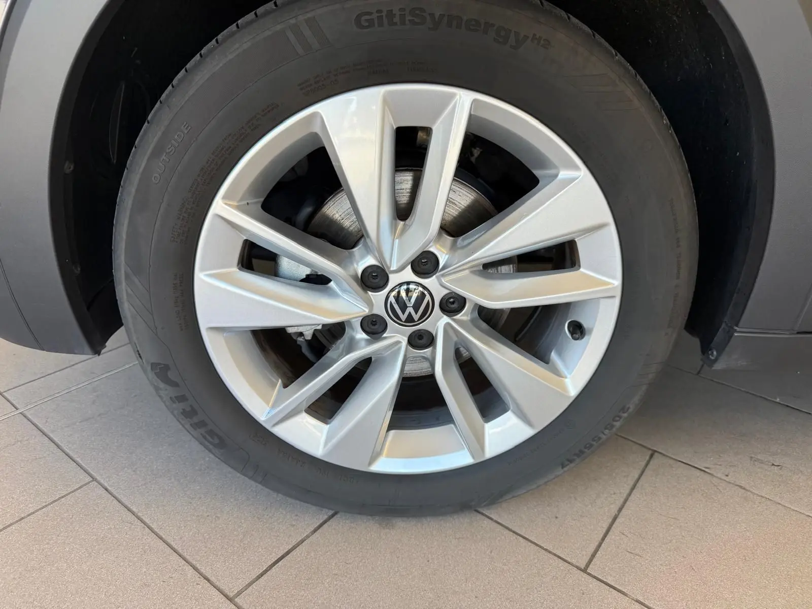 Gros plan sur la roue avant droite du Volkswagen T-Cross gris cendre 2025 avec jante alliage à dix branches.