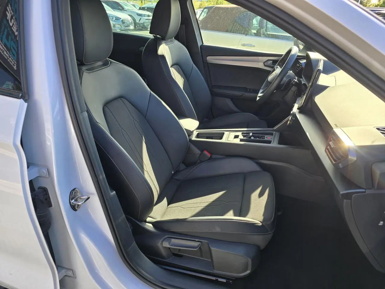 Vue intérieure côté conducteur d'une CUPRA Leon Sportstourer blanche Nevada, sièges noirs et tableau de bord moderne.