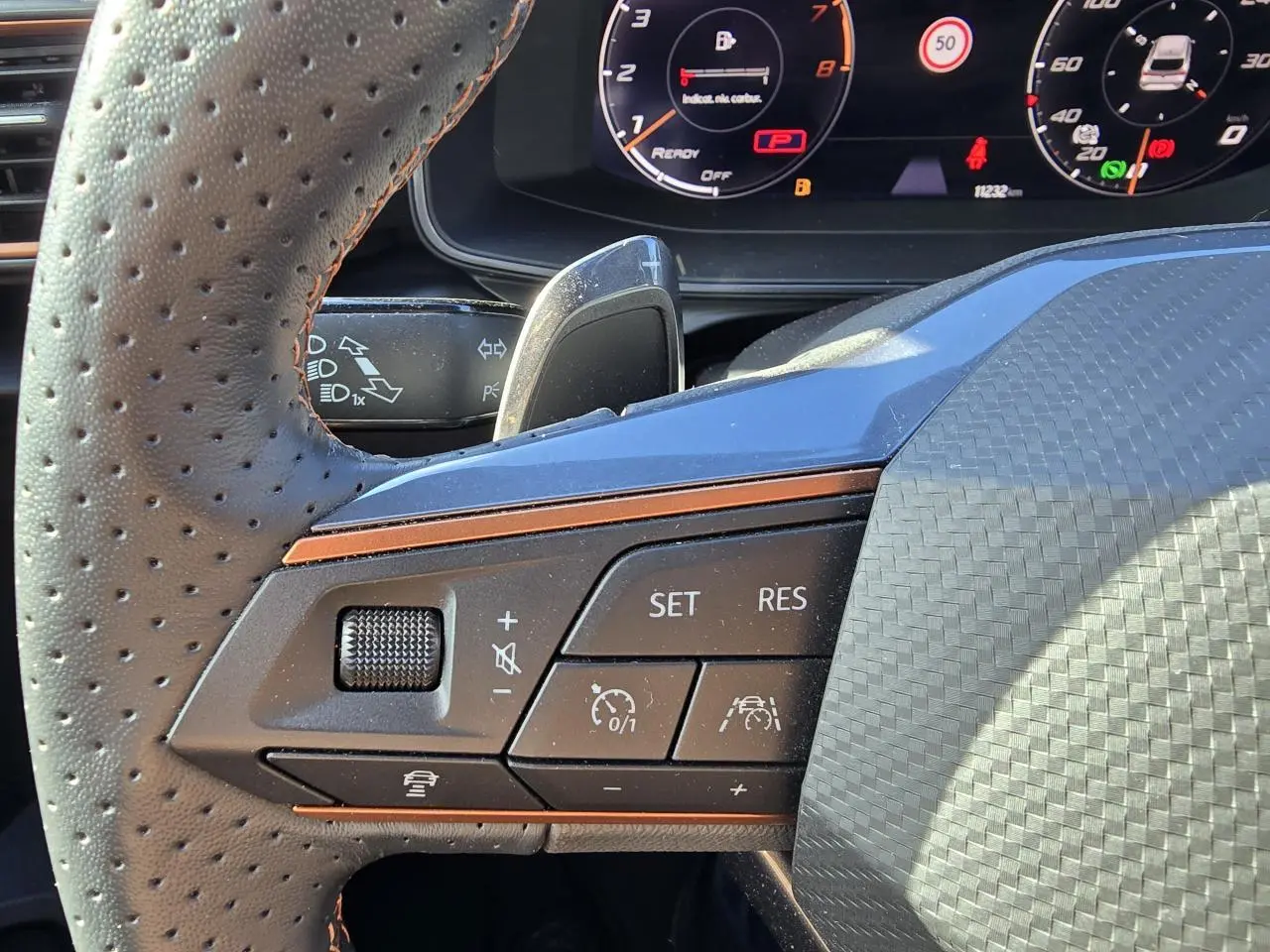 Gros plan sur les commandes du volant en cuir perforé du Cupra Leon Sportstourer blanc Nevada, avec combiné digital visible.